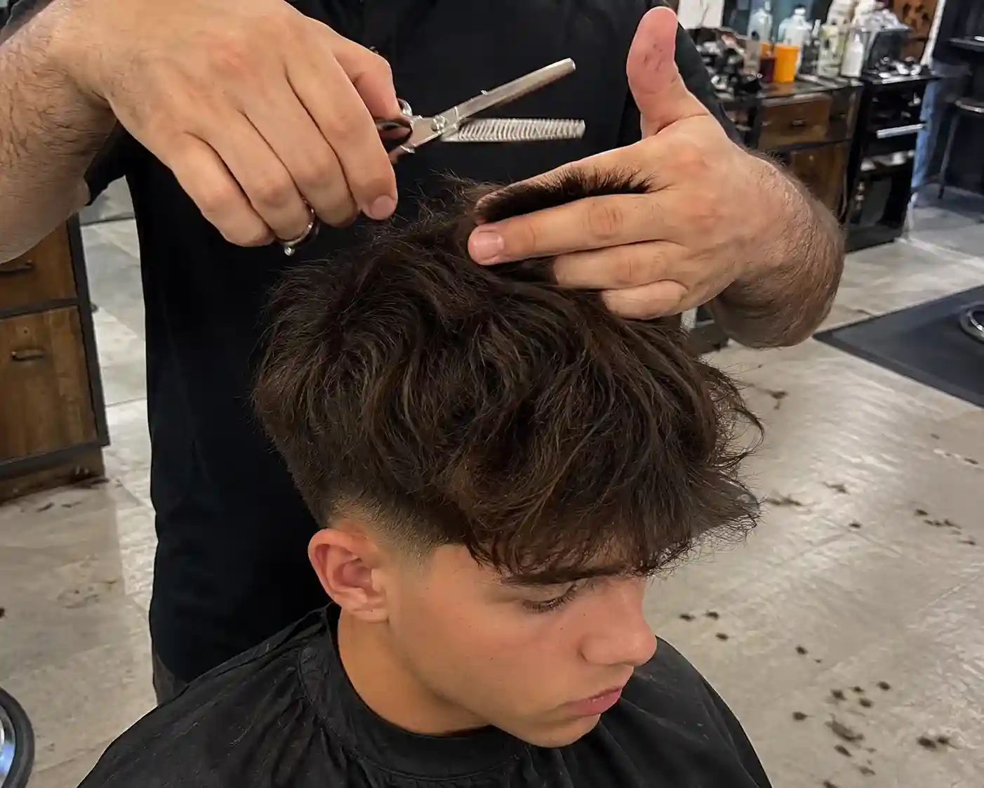 Friseur dünnt mit der Effilierschere dickes Haar eines Jugendlichen für eine moderne Frisur für Jungs aus