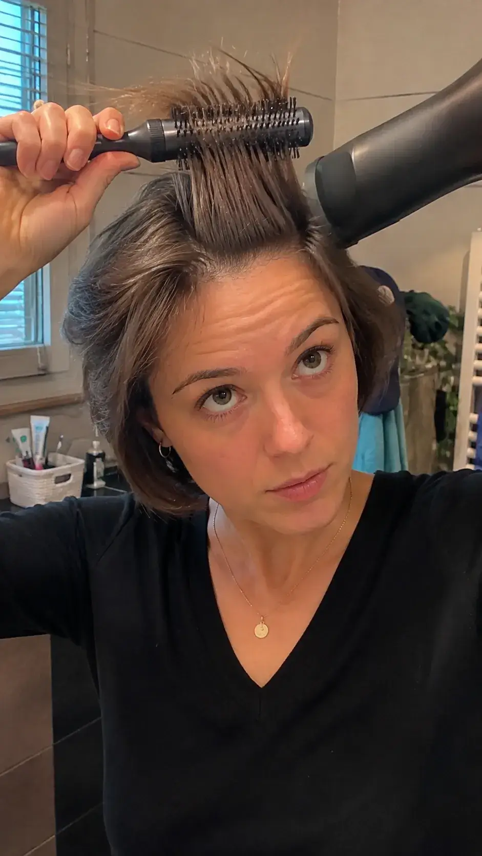 Frau föhnt kurze Haare mit Rundbürste für mehr Volumen an den Wurzeln