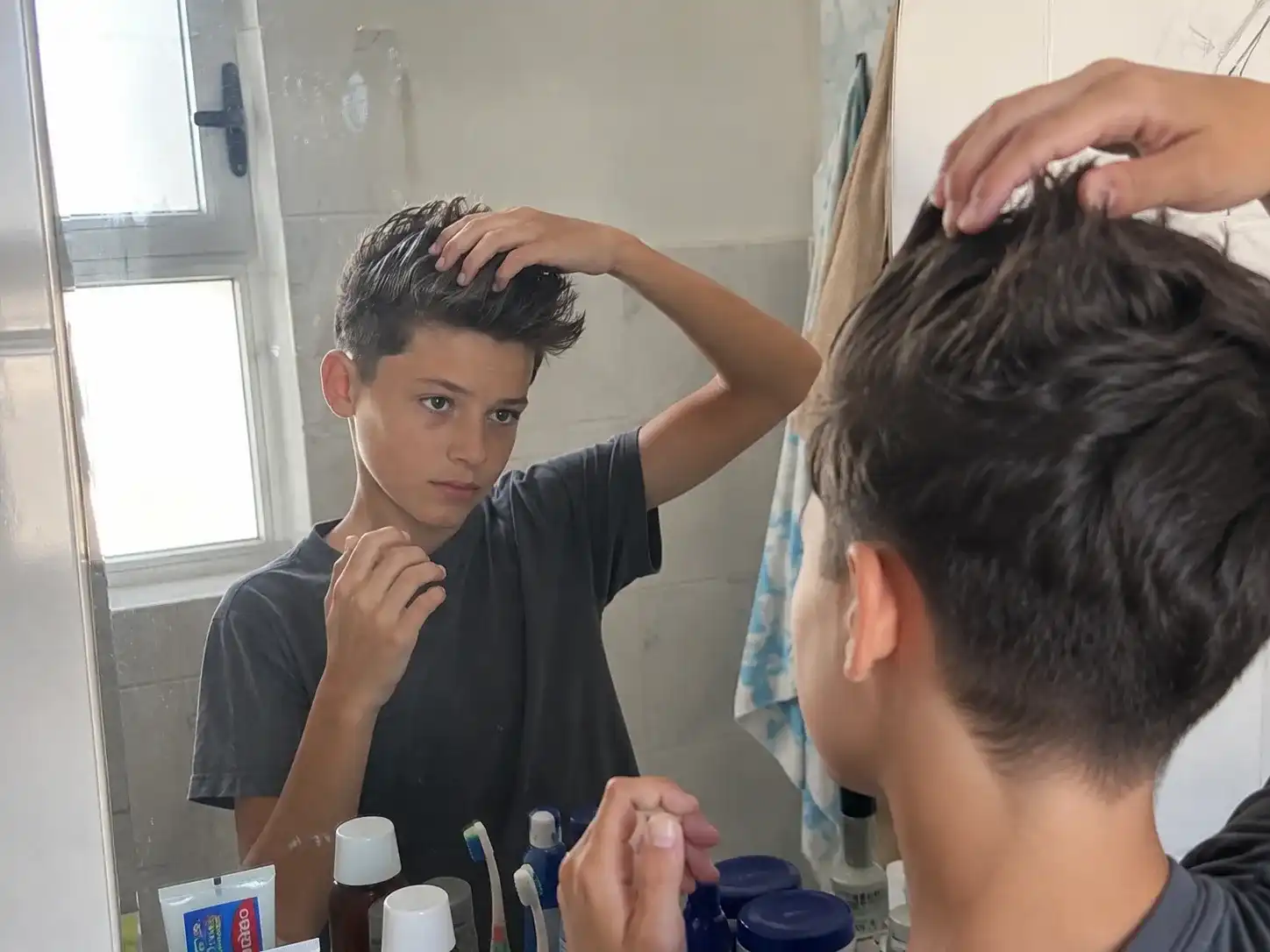 13-jähriger Junge stylt sein Deckhaar mit etwas Wachs zum Quiff vor dem heimischen Badezimmerspiegel