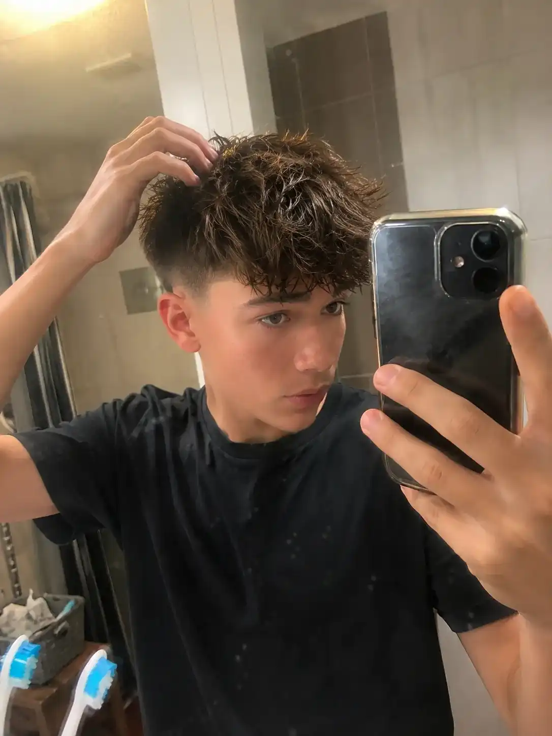 Teenager lässt sich im Spiegel einen Undercut mit längerem Deckhaar stylen, beliebt bei coolen Frisuren für Jungs ab 13